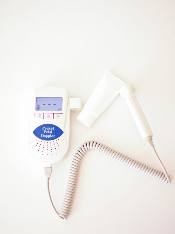 A fetal doppler with unmarked bottle of ultrasound gel on white table.