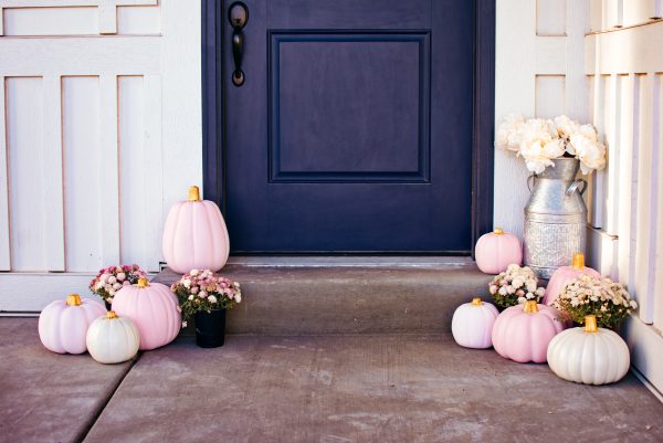 Painted pink pumpkins arranged on front porch with containers of mums and tin milk jug.