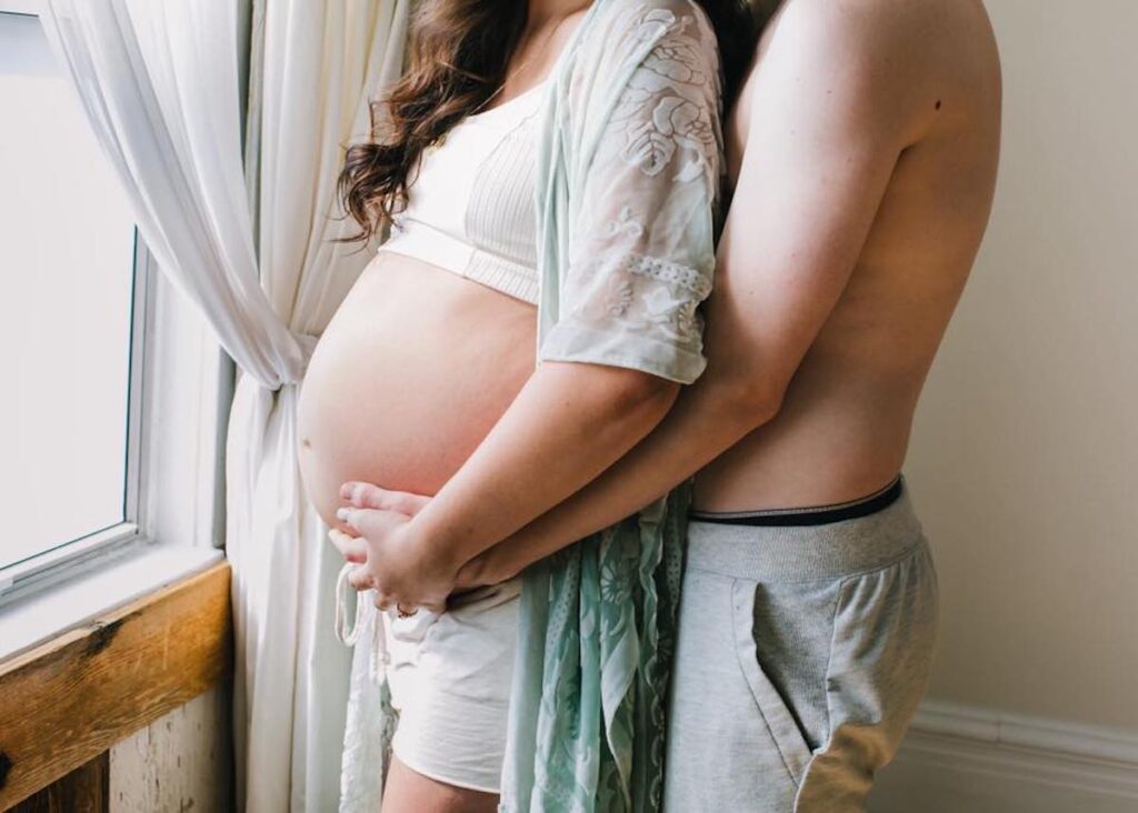 Husband and wife touch hands on baby bump during in home maternity pictures.