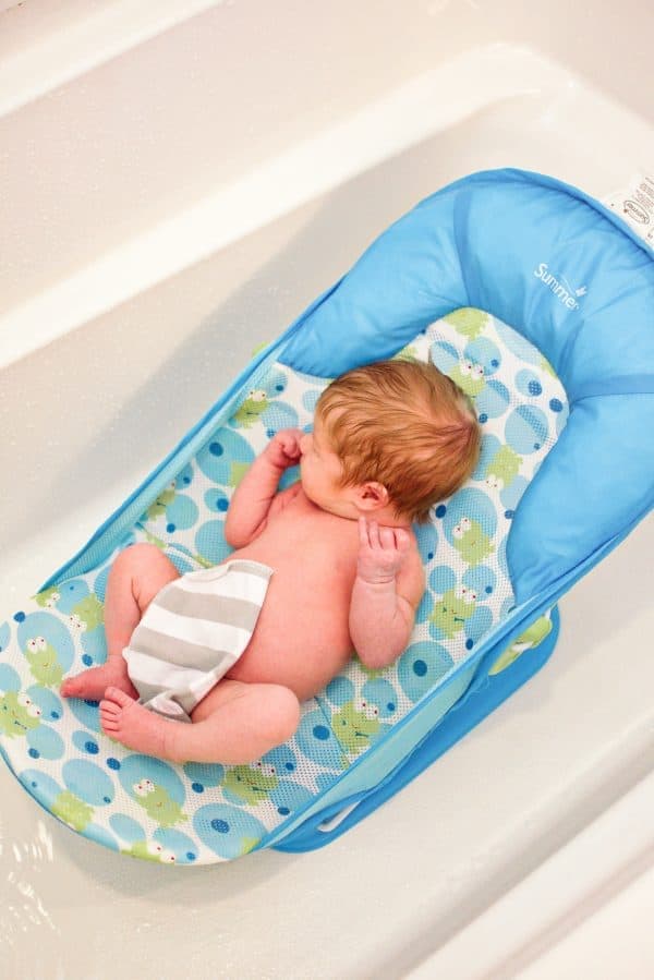 Baby sits in bath chair with washcloth on tummy. 