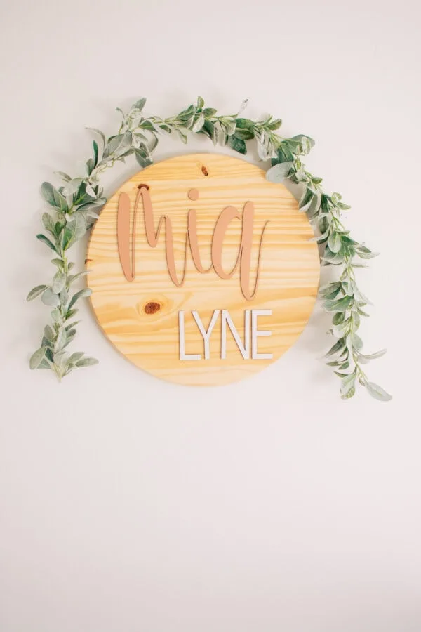 Wooden name sign hangs as part of some baby room decor.