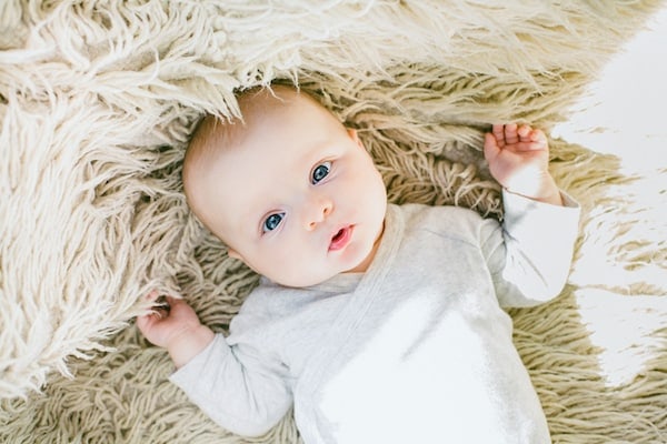 Baby with a gender neutral name lays on a rug.