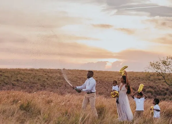 Family walks through a grassy area holding number balloons.