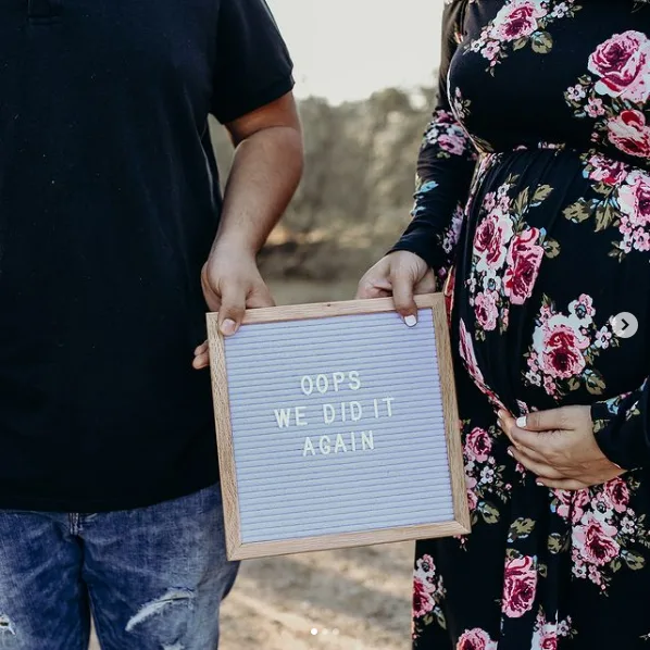 Husband and wife hold up letter board baby announcment.