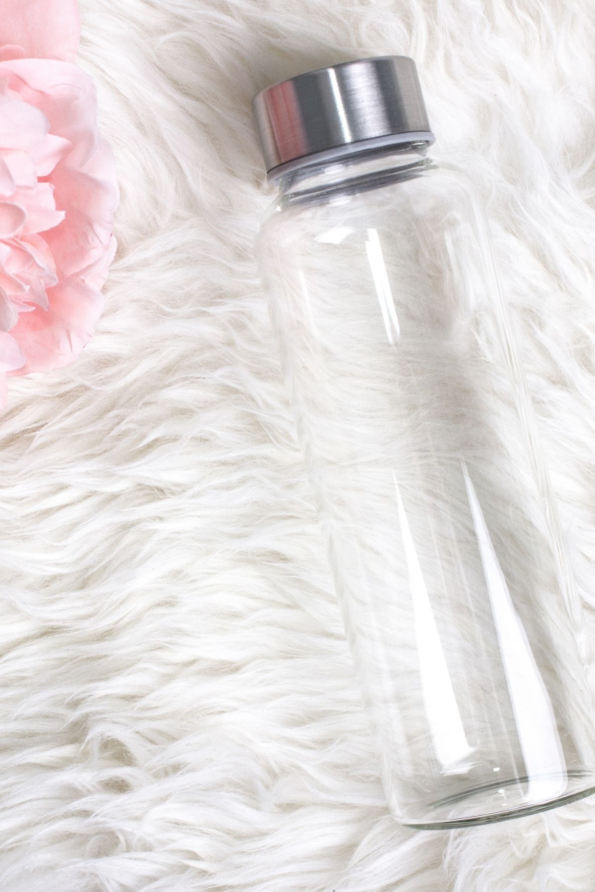 Clear water bottle on white fur rug with pink flower in top left corner.