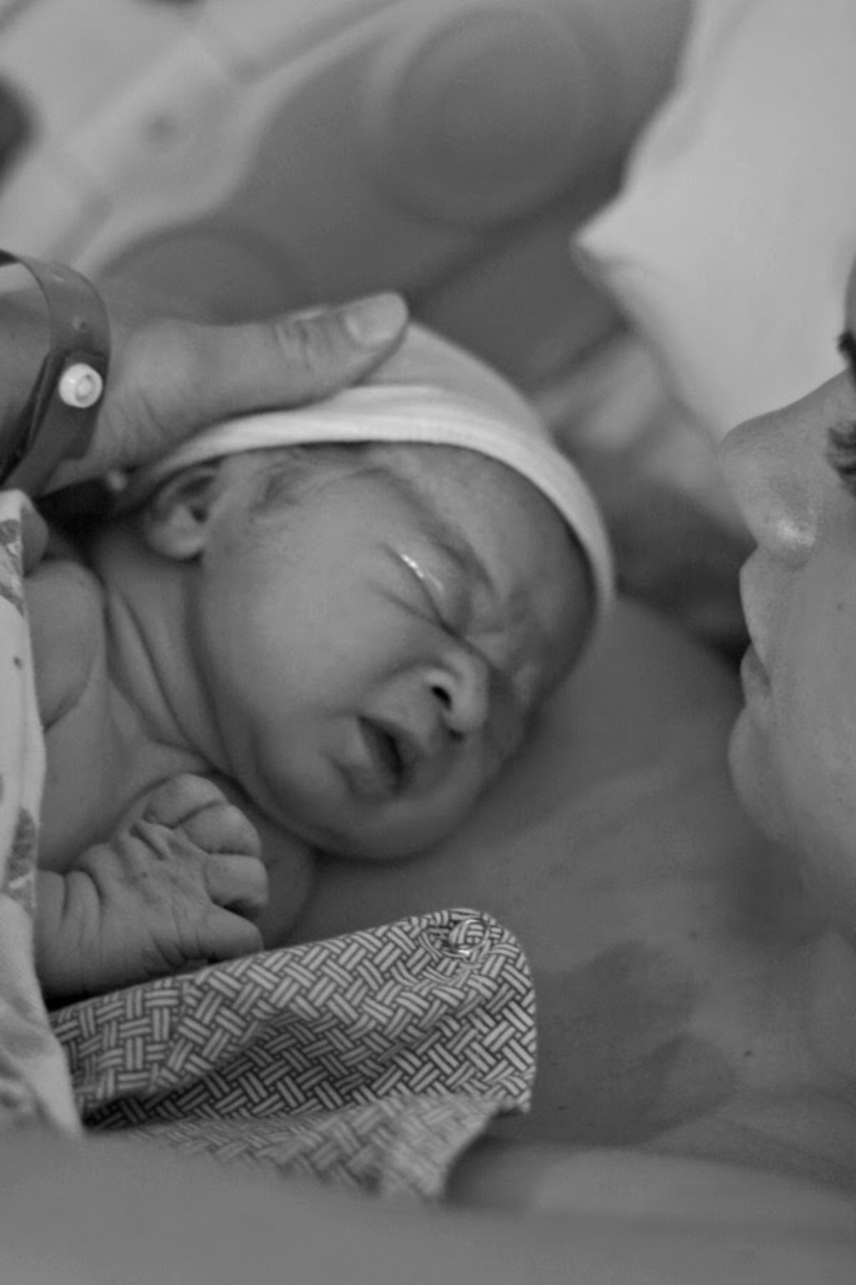 Black and white photo of woman holding baby boy wearing hat after delivery.