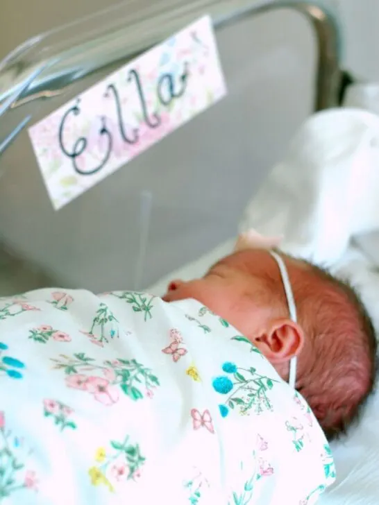 Newborn baby sleeps in her bassinet labeled with her baby name sign, 
