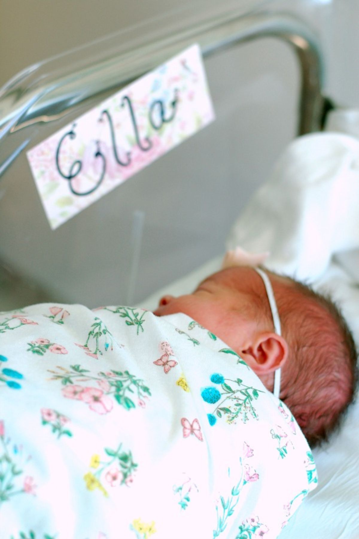 Newborn baby sleeps in her bassinet labeled with her baby name sign, "Ella." 