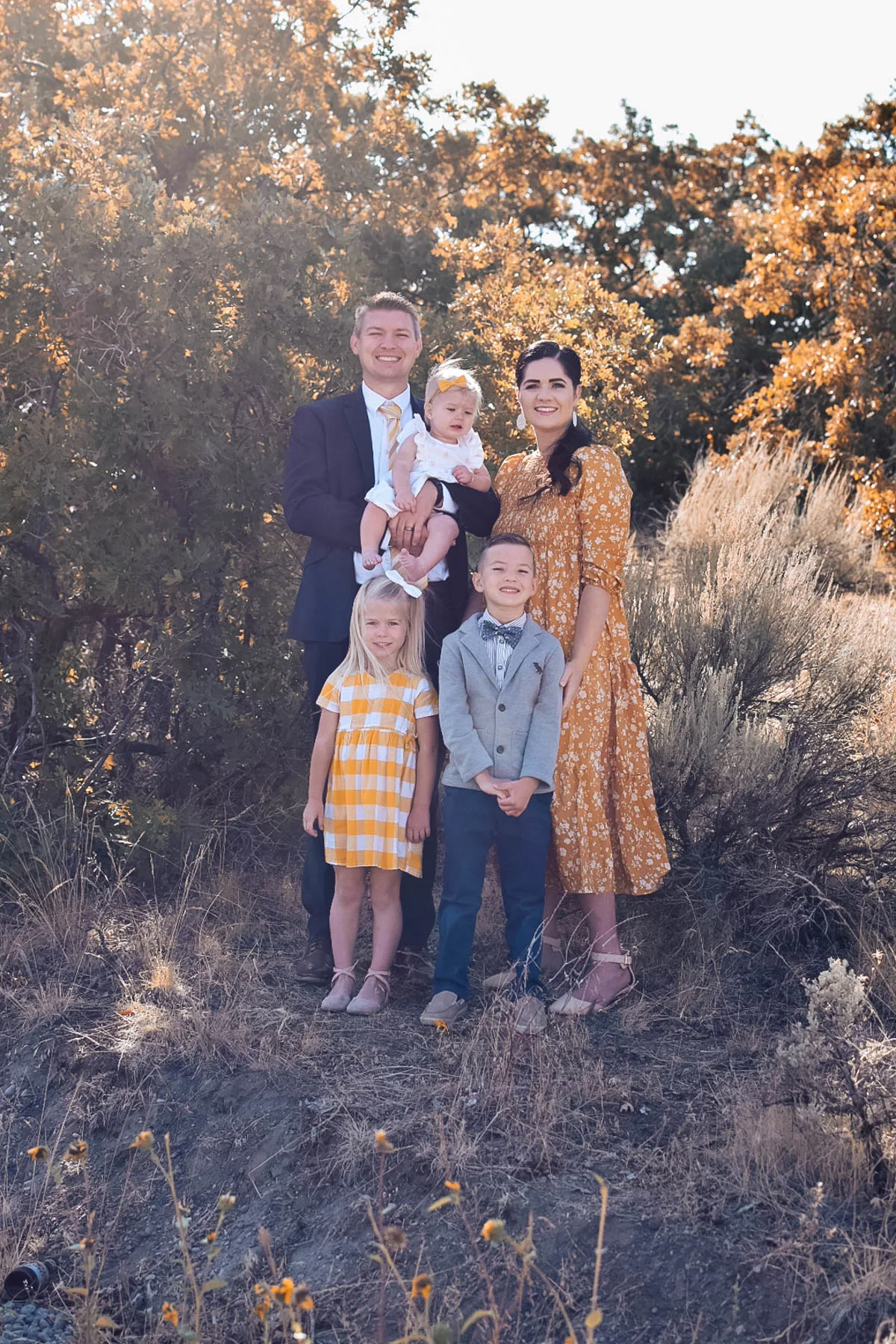 Family of 5 wearing yellow and blue outfits stands by tree with yellow leaves for family pictures.