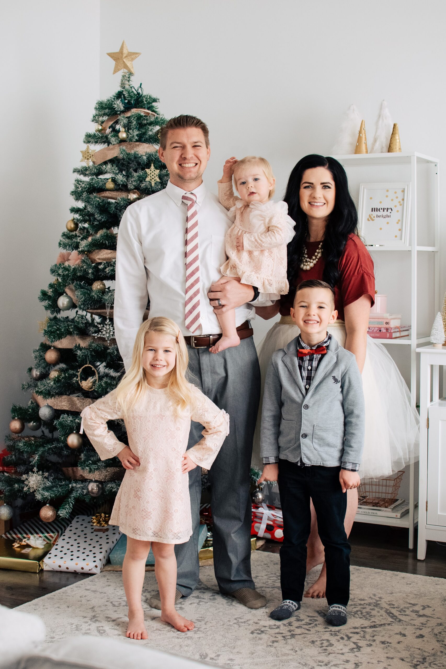 Family of 5 wearing red and white dress clothes stand in front of Christmas tree.