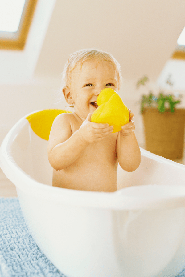 Baby boy plays in the tub with a rubber duck.