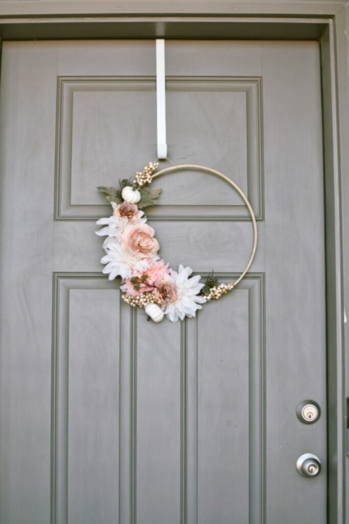 Wooden hoop wreath with pink and cream flowers hangs on gray front door.