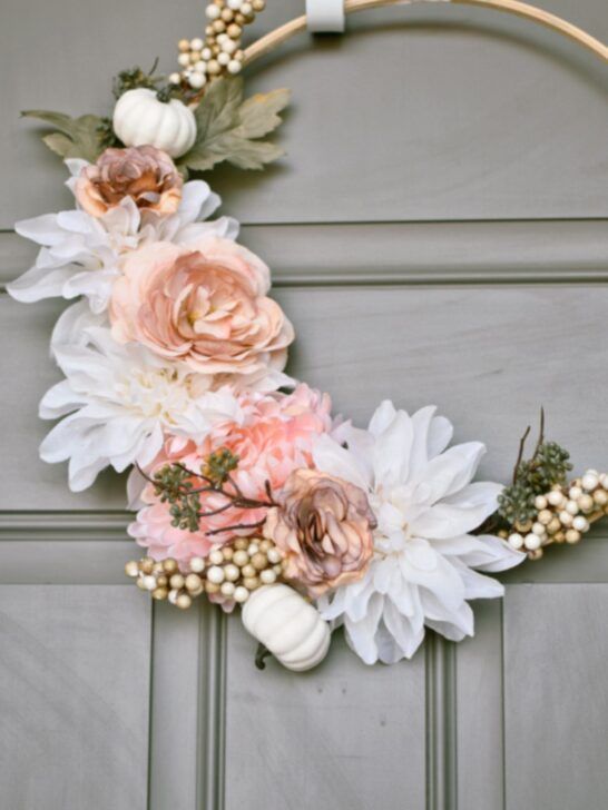 Wooden hoop wreath with pink and cream fall flowers hanging on gray door.