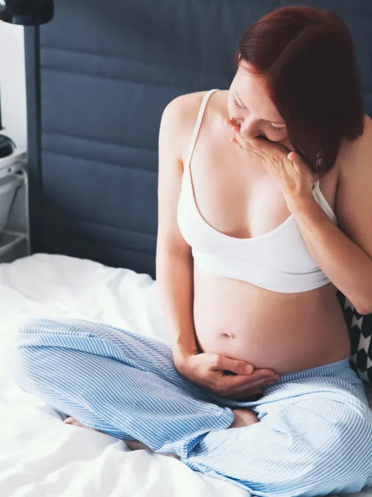 Pregnant woman holds belly while experiencing early pregnancy symptoms.