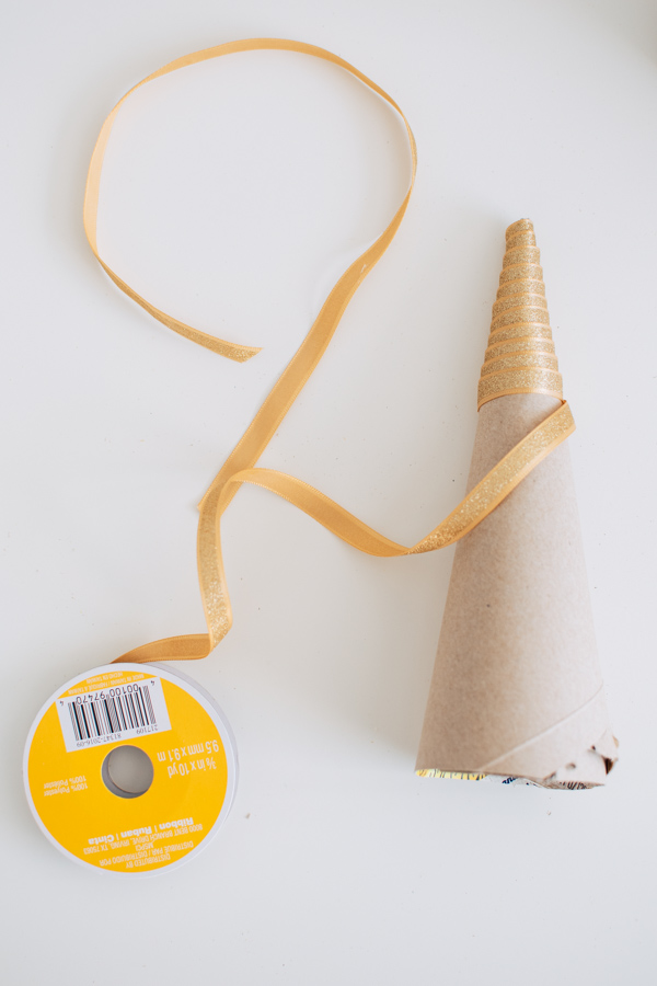 DIY cone Christmas tree with gold ribbon on part of it laying on white table.