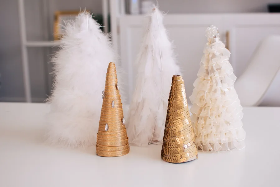 Five DIY Christmas cone trees decorated with white feathers, gold ribbon, and cream ribbon on a table