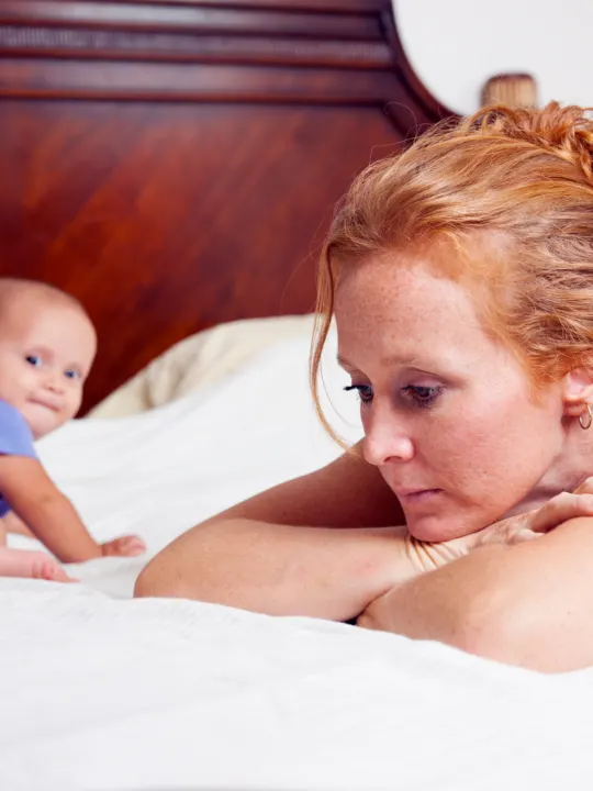 Frustrated mother lays on bed with baby.