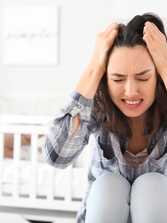 Women holds head in frustration as she deals with postpartum depression.