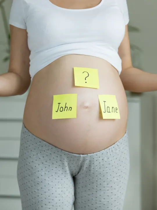 Woman displays pregnant belly with yellow baby name sticky notes.