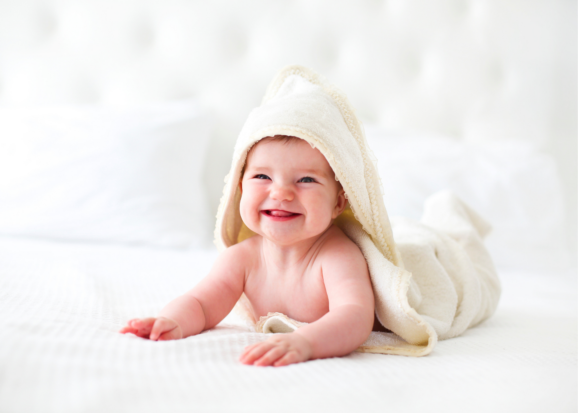 Baby smiles while wearing hooded towel on bed.