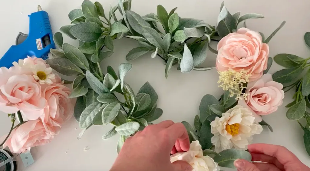 Woman puts faux flowers on a heart shaped wreath.