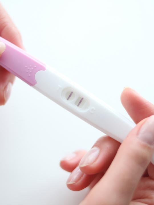 Female hands hold pink, positive pregnancy test