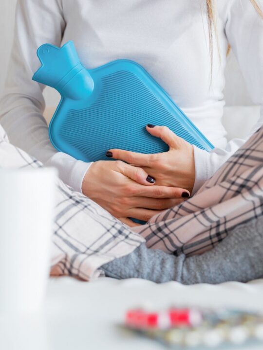 Woman holds blue heating pad to stomach while experiencing uncomfortable postpartum bleeding.