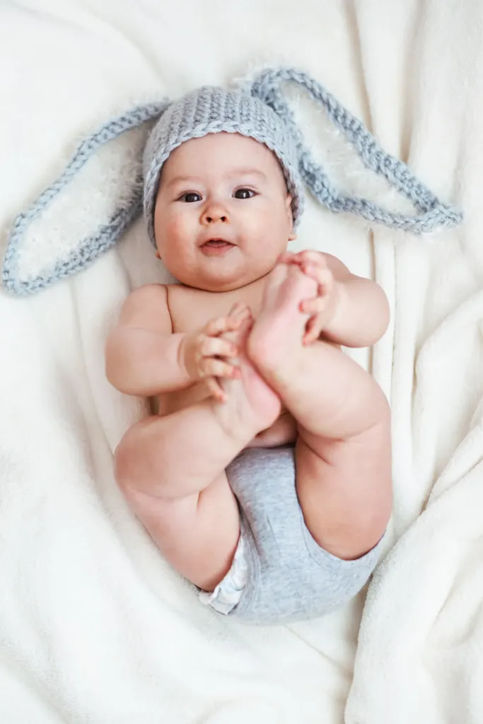 Baby boy with a bunny hat grabs his feet.
