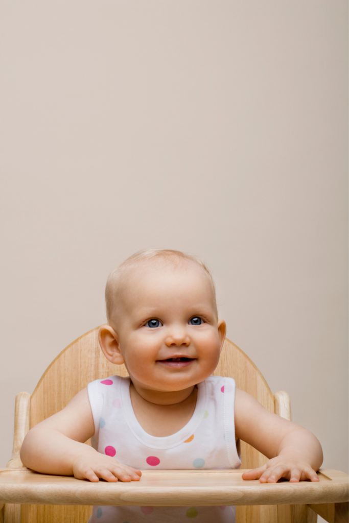 Baby girl smiles while sitting in a high chair.