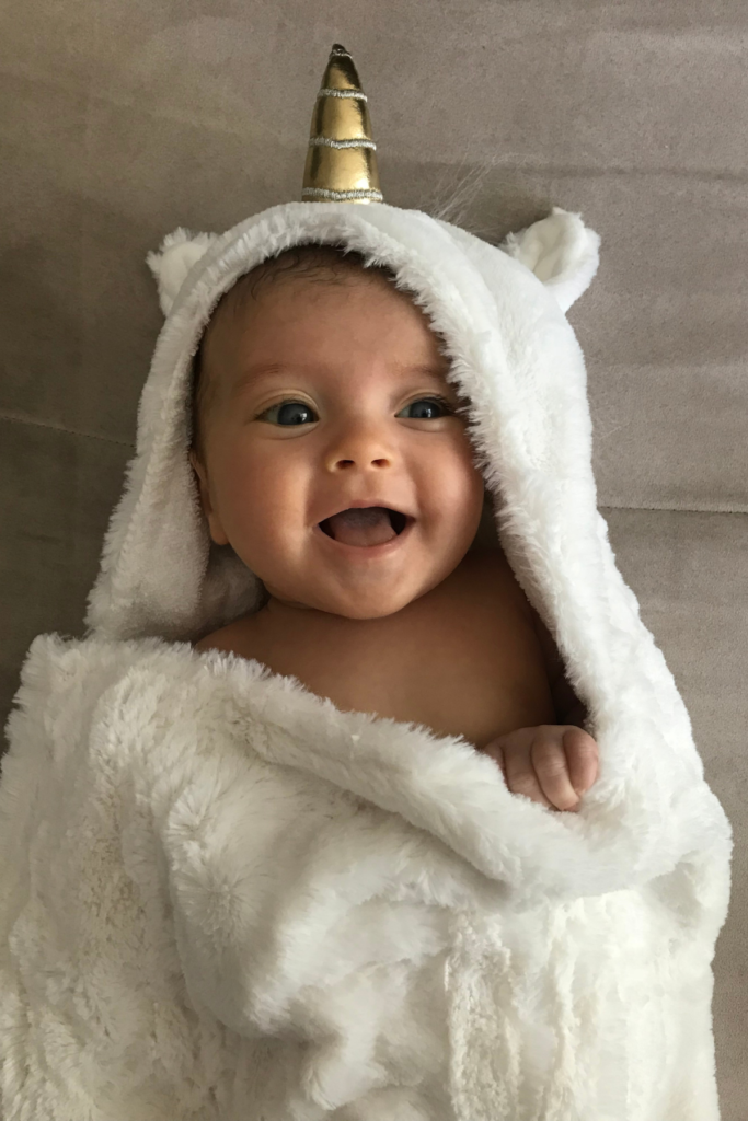 Baby girl wears a hooded unicorn towel.