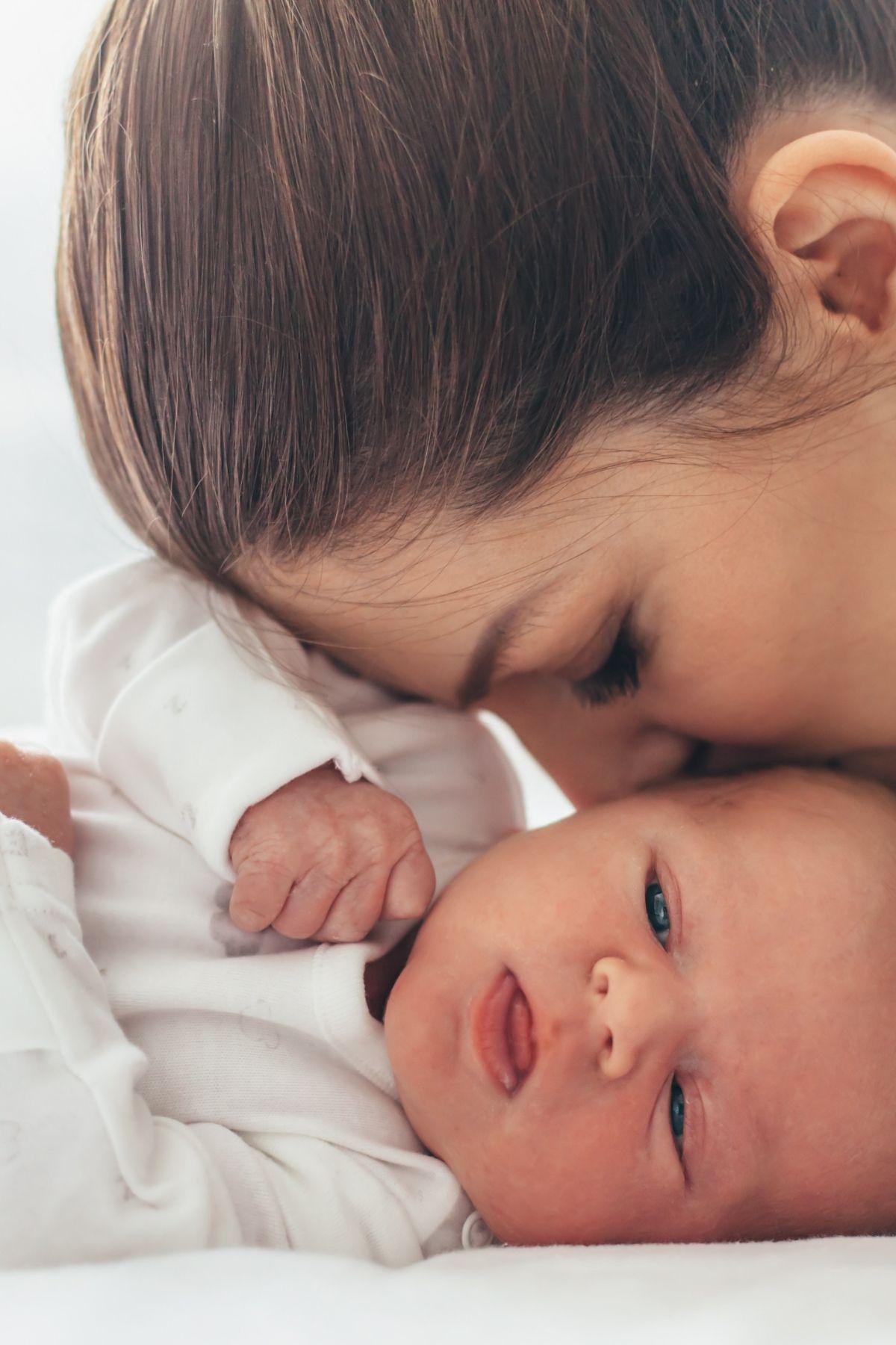 Close up of woman leaning over to gently kiss newborn baby's face.