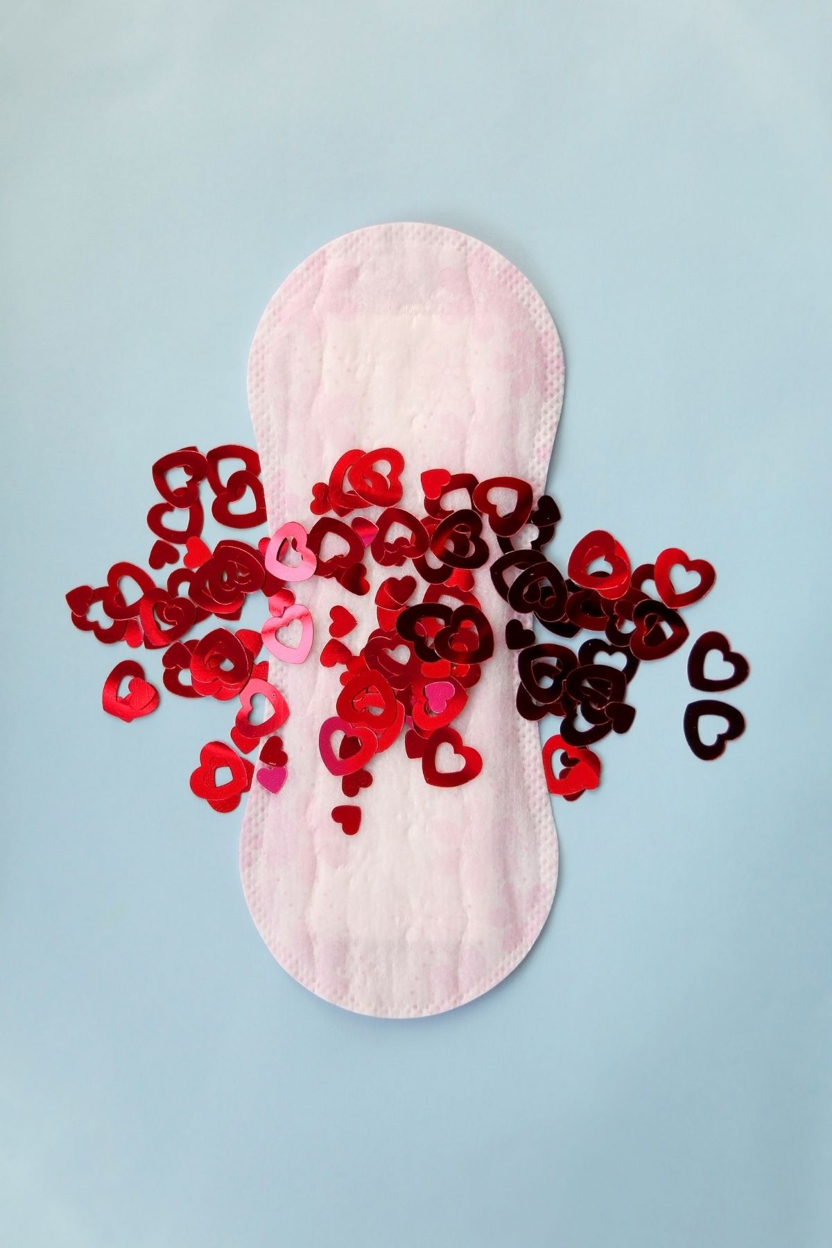 Sanitary pad with tiny red heart cutouts scattered over surface to represent blood.