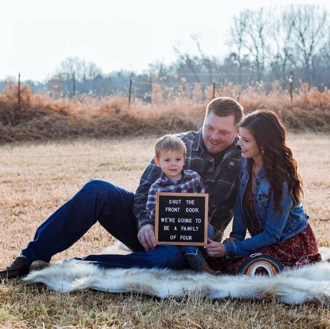 Family sits on blanket and holds black letter board.