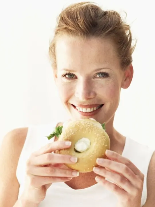 Woman eats cream cheese bagel sandwich.