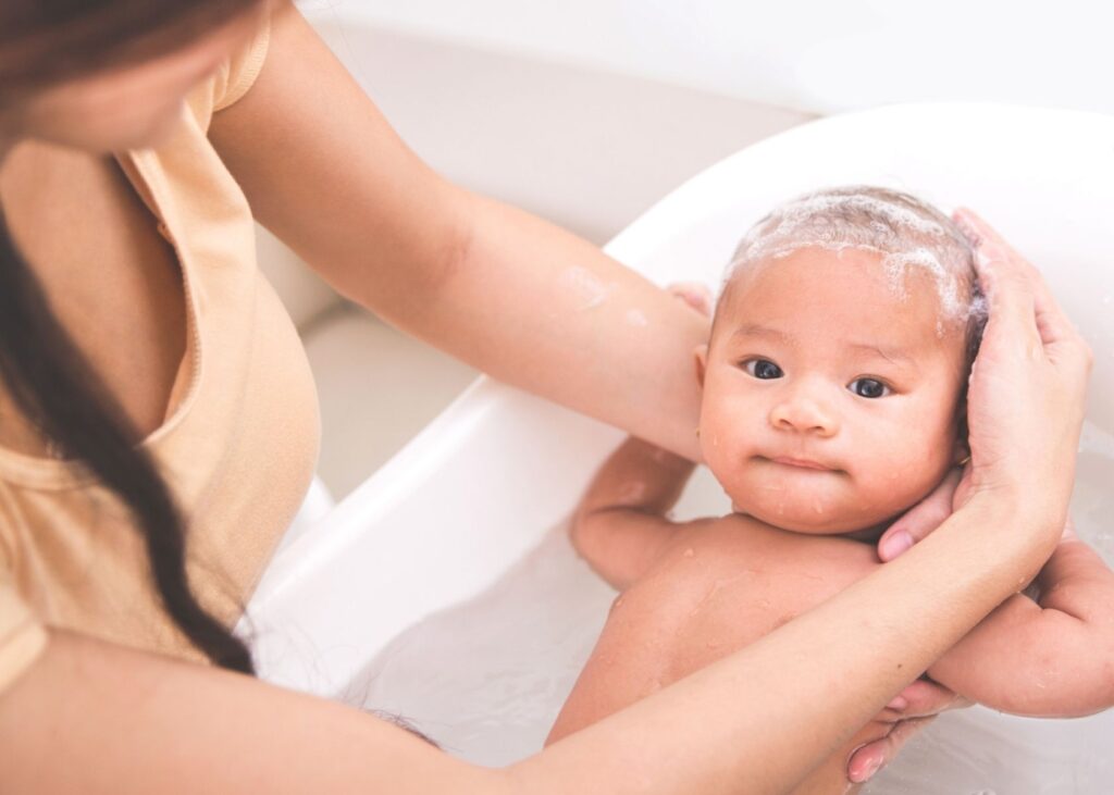 Newborn gets hair washed in bathtub.