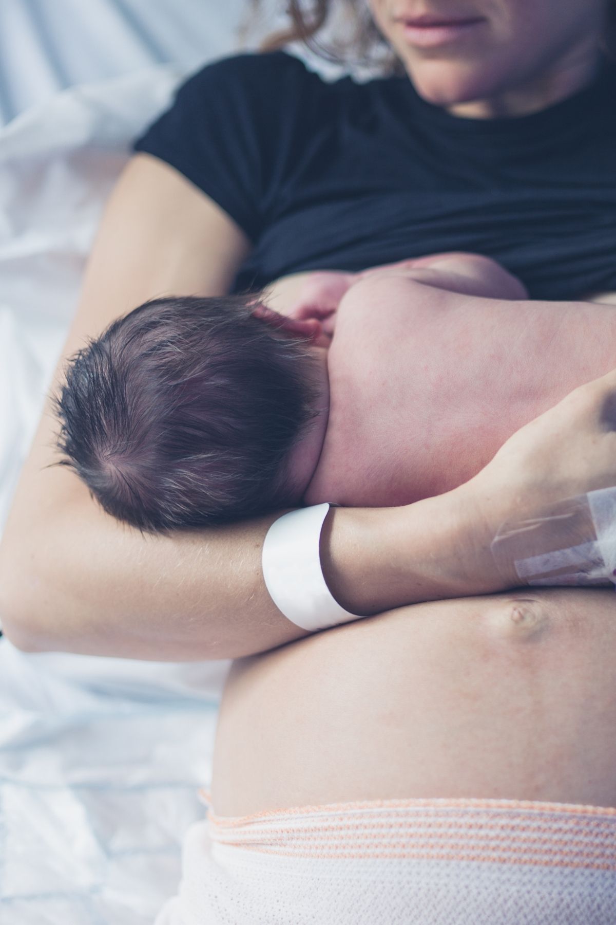 New mom breastfeeds newborn in hospital bed.