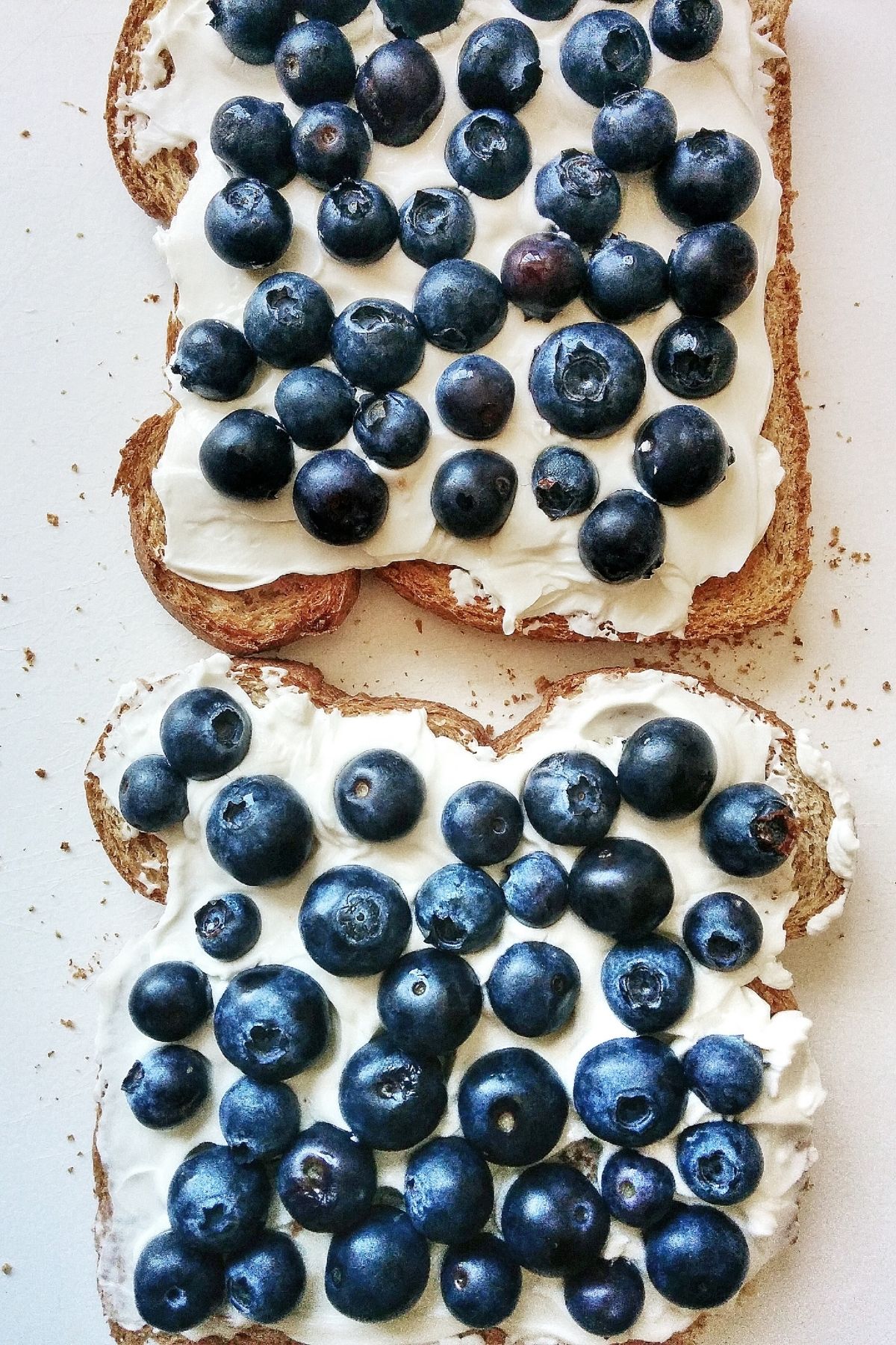 Two pieces of toast with cream cheese spread and blueberries on top.