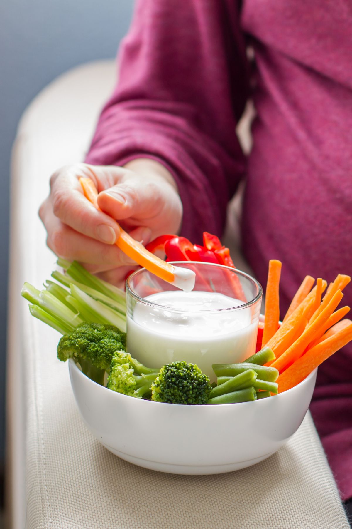 Pregnant woman in purple shirt Dips a carrot stick into sour cream dip.