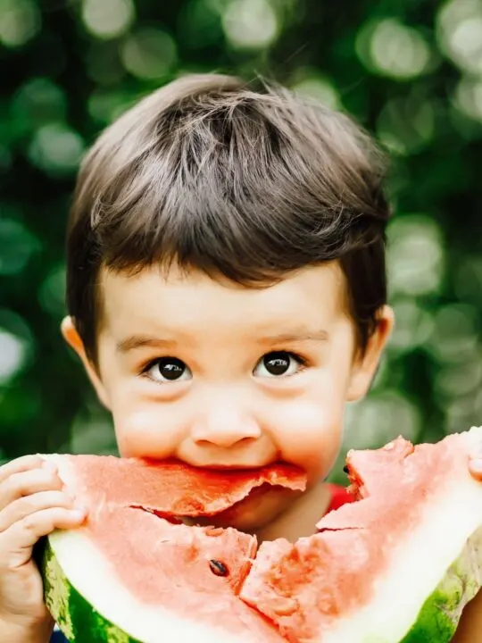Little boy eats watermelon outside.