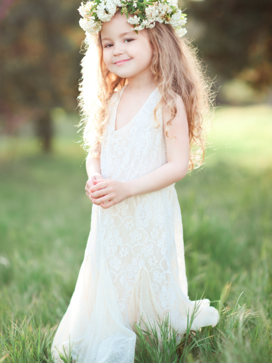 Little girl stands outside in white dress and flower crown.