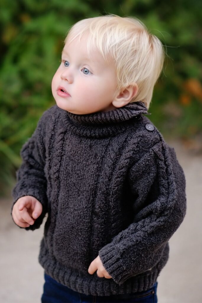 Little boy stands outside in black knit sweater.