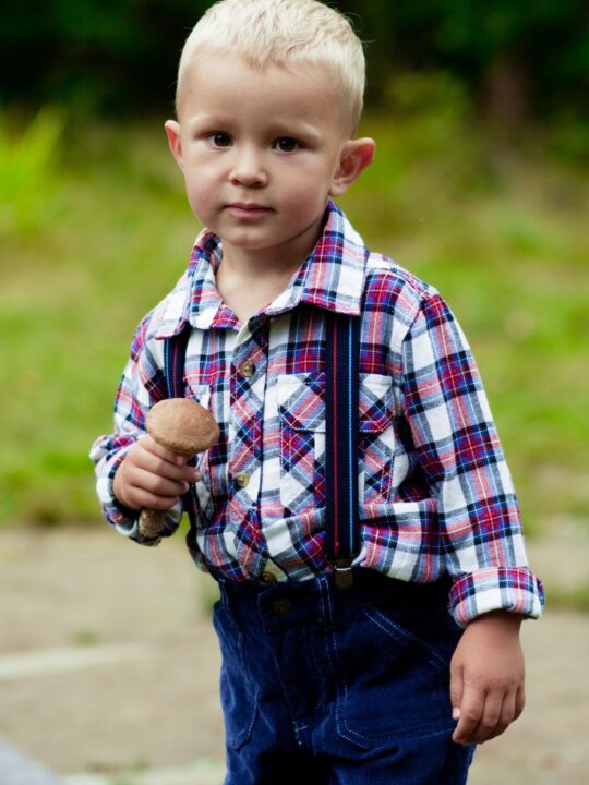 Little boy stands outside in suspenders.