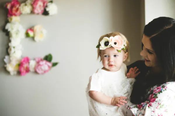 A mom holds a toddler girl in a white tulle dress with a floral headband.