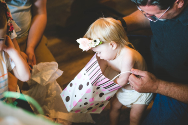 A grandfather helps his toddler granddaughter open presents.