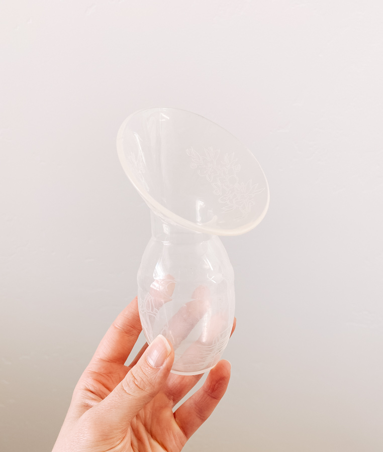 Woman holds silicone breast pump against a white wall.