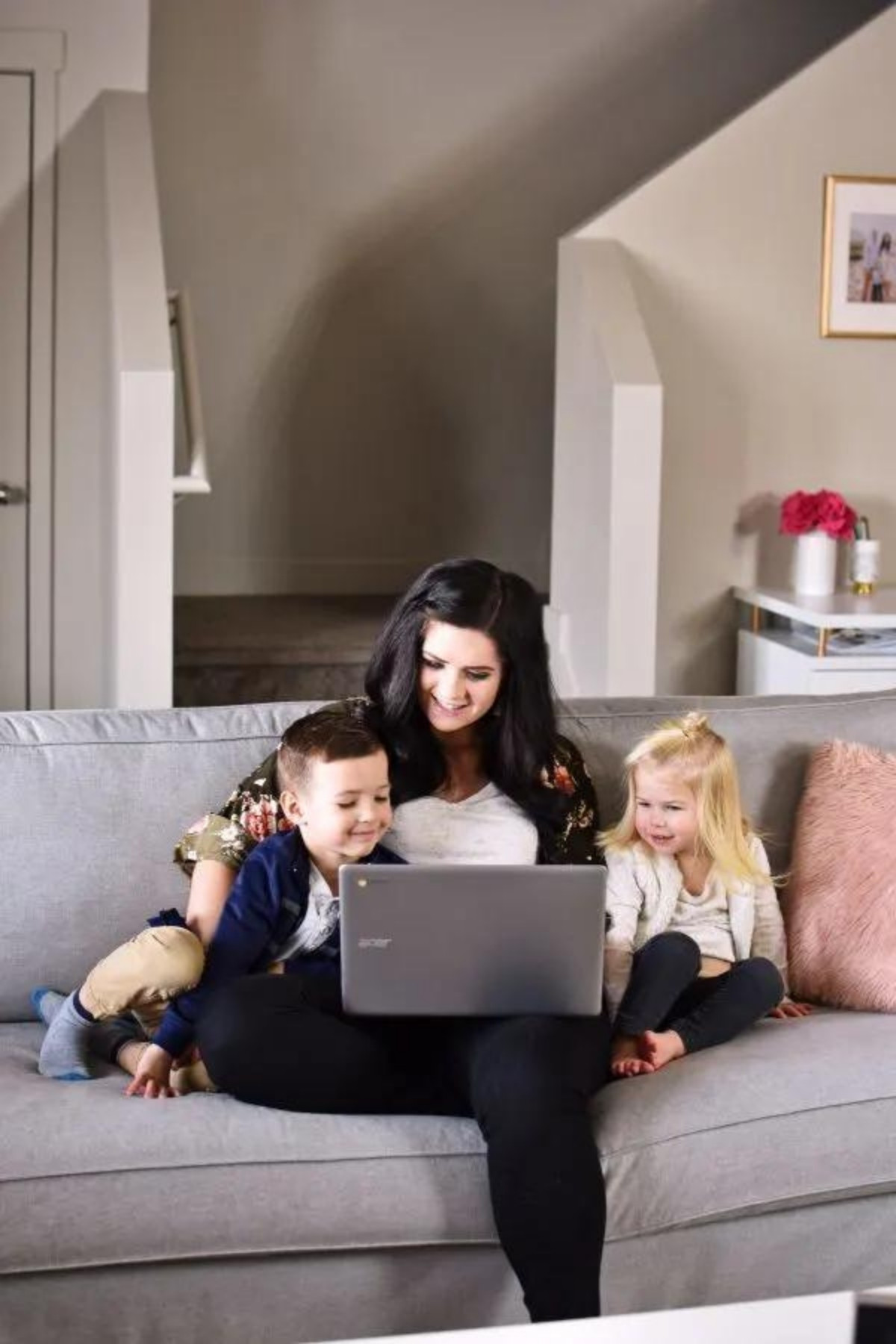 Woman sits on couch with boy and girl on either side of her and a computer on her lap.