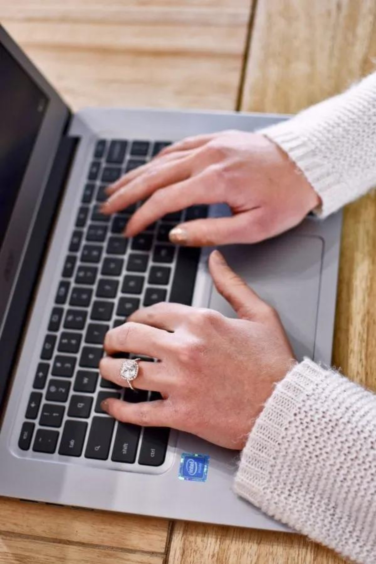 Woman's wearing a diamond ring and nail polish types on laptop computer.