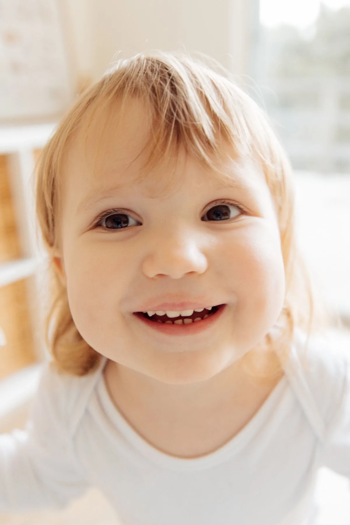 Close up photo of blonde girl with brown eyes wearing a white onesie and smiling.