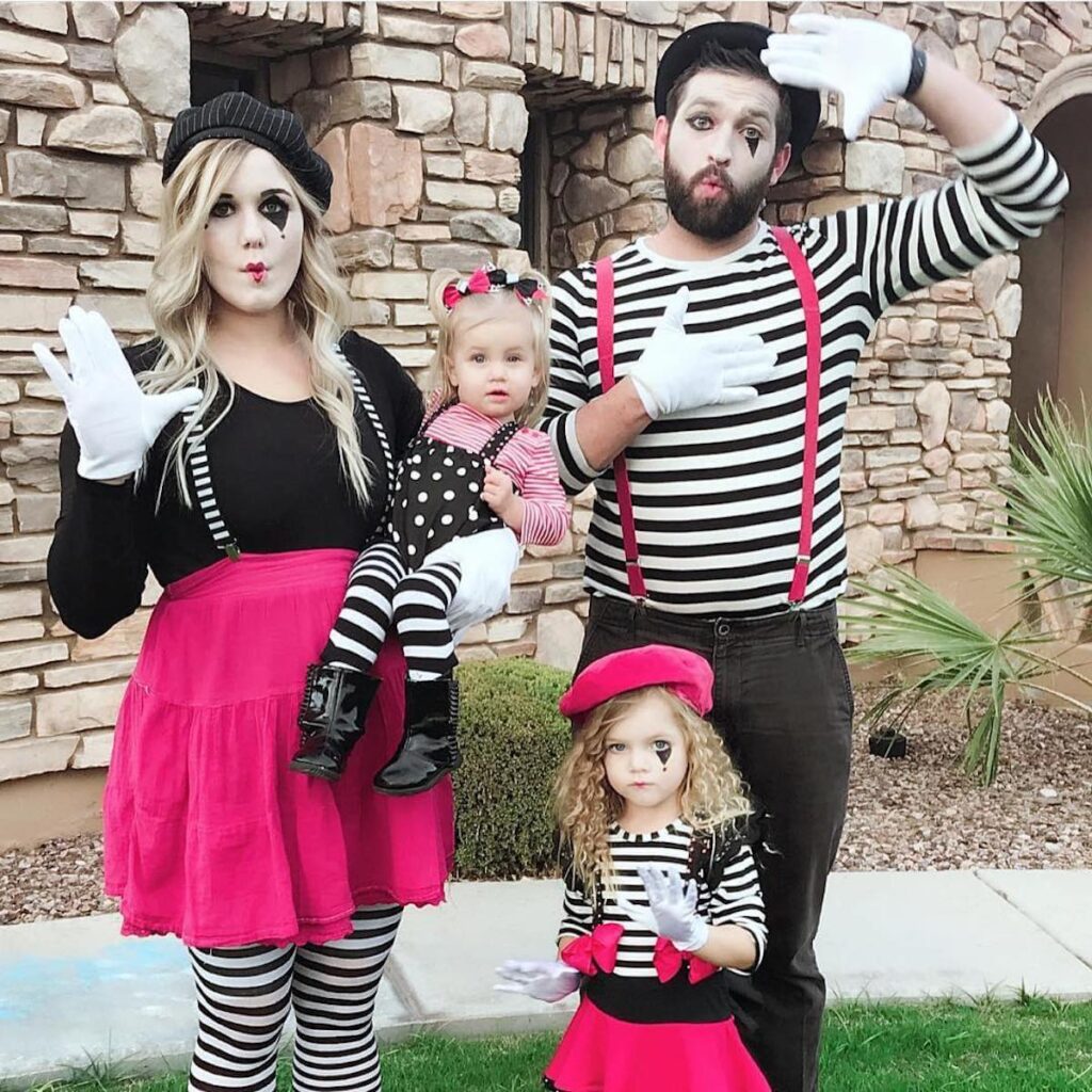Family poses while wearing pink and black mime costumes.