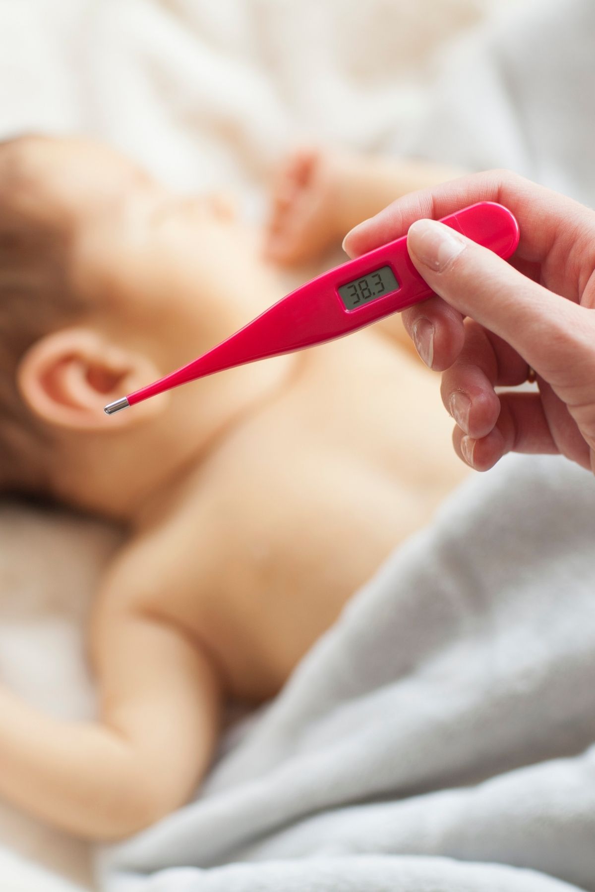 Mother checks her sick newborn baby's temperature with a red thermometer while baby sleeps.